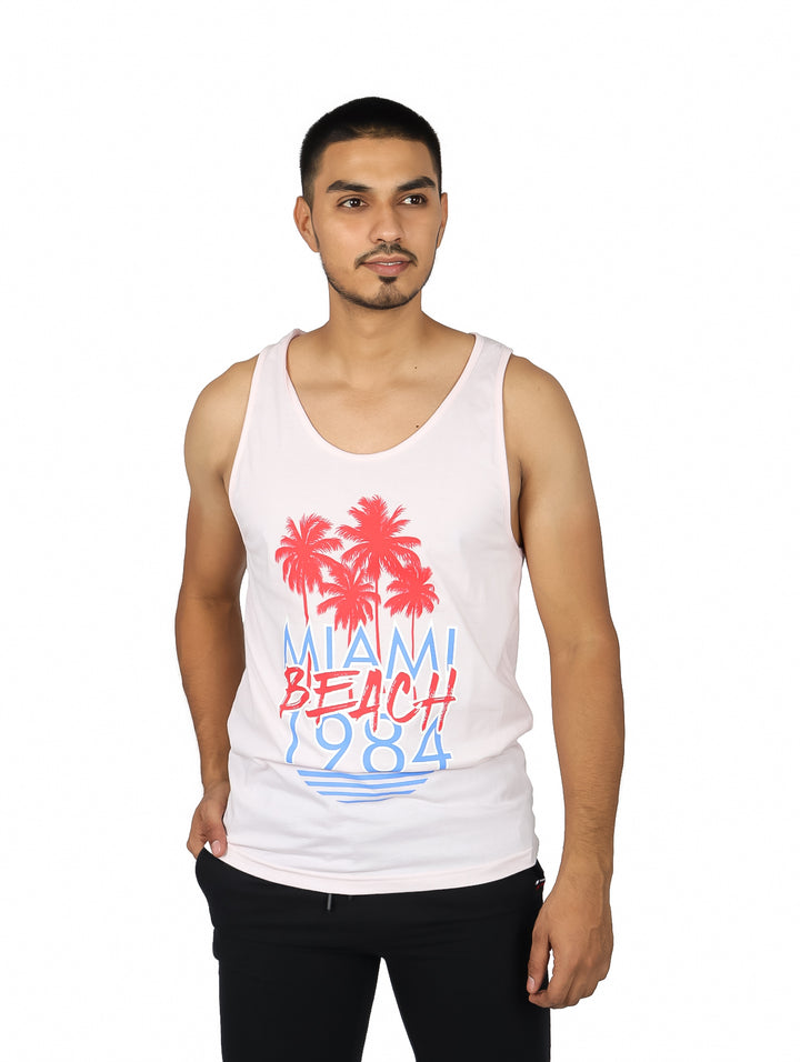 Hombre vistiendo playera tank rosa con estampado de palmeras y texto Miami Beach 1984 en rojo y azul.