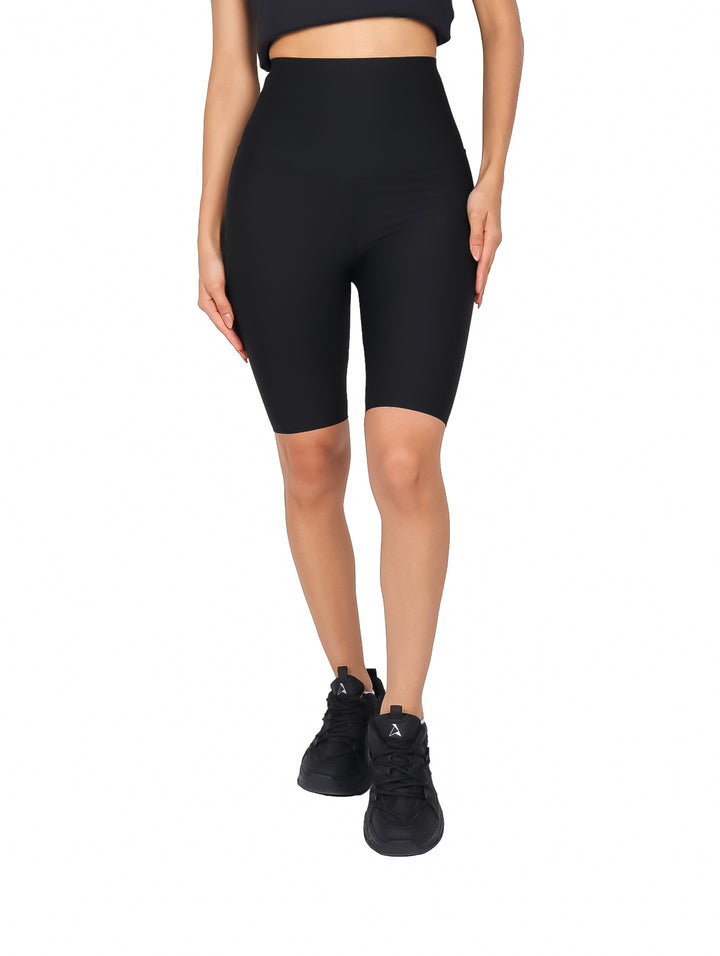 Mujer vistiendo biker shorts negros de cintura alta y calzado deportivo negro sobre fondo blanco.