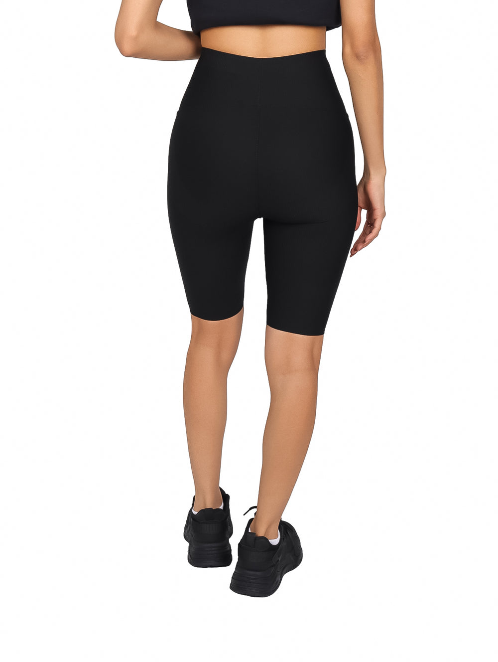 Mujer vistiendo biker shorts negros de cintura alta y calzado deportivo negro sobre fondo blanco.