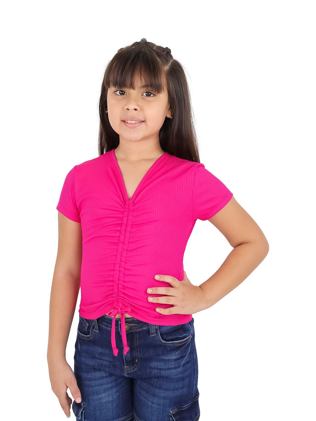 Niña con camiseta fucsia ajustada con detalle fruncido al frente y pantalones vaqueros.