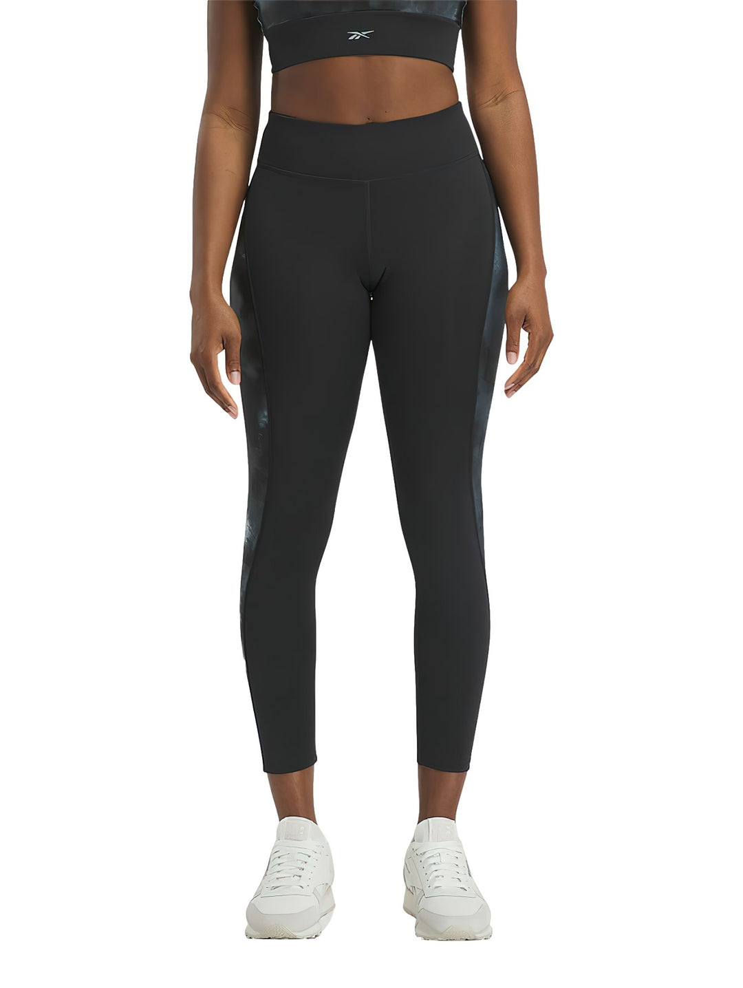 Mujer vistiendo mallas deportivas Reebok negras con detalles laterales brillantes.