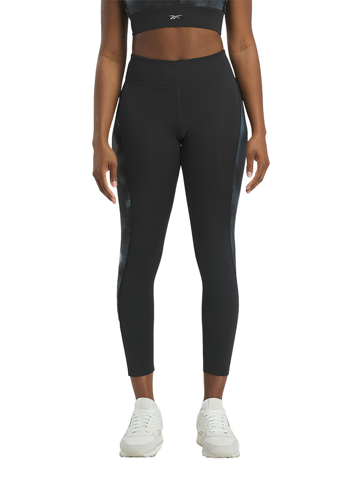 Mujer vistiendo mallas deportivas Reebok negras con detalles laterales brillantes.