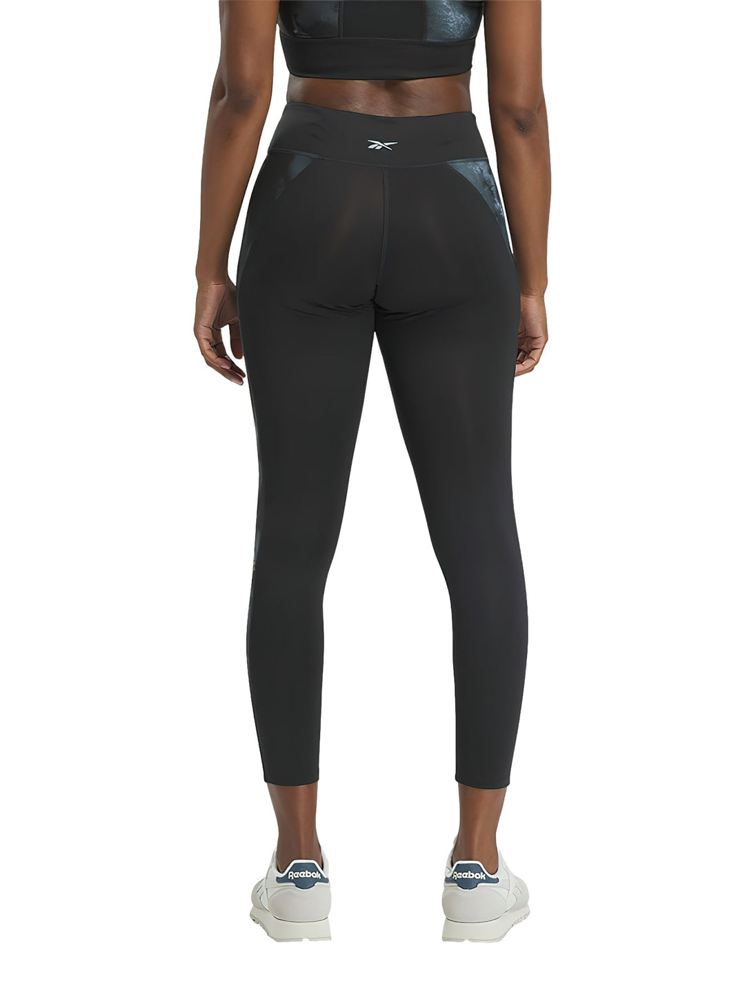 Mujer vistiendo mallas deportivas Reebok negras con detalles laterales brillantes.