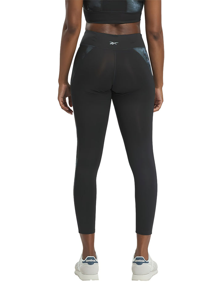 Mujer vistiendo mallas deportivas Reebok negras con detalles laterales brillantes.