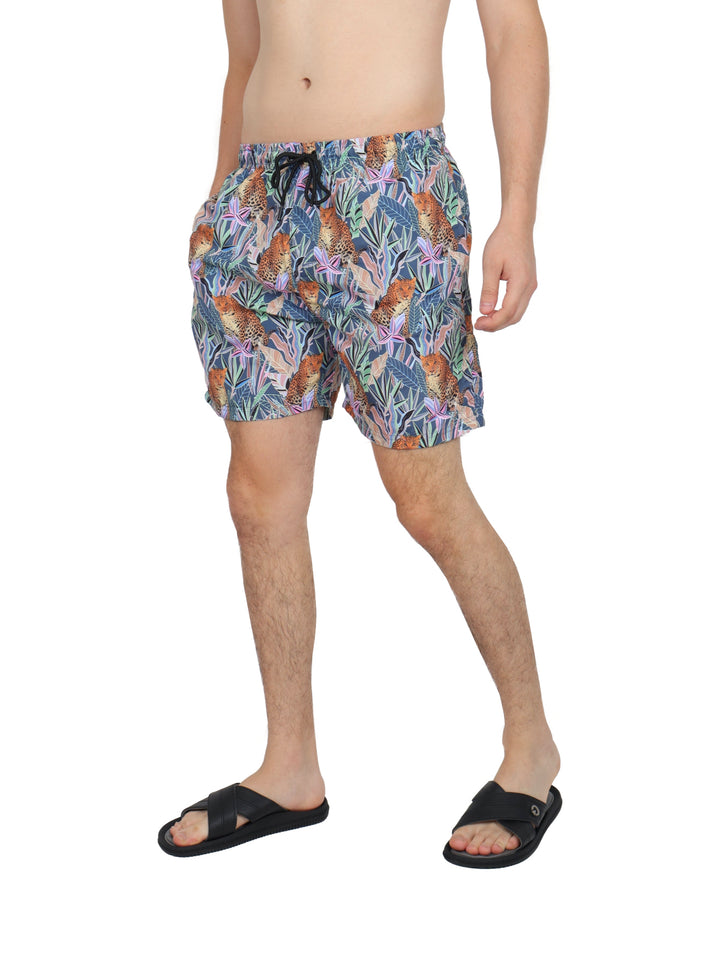 Hombre vistiendo traje de baño corto multicolor con estampado de jaguares y hojas tropicales.