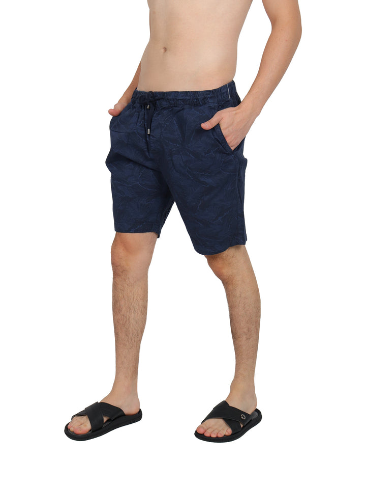 Hombre vistiendo bermudas color marino con estampado sutil de hojas y cordón en la cintura.