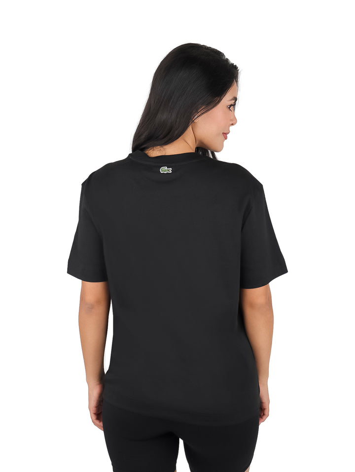 Mujer vistiendo blusa básica negra de manga corta marca Lacoste y shorts negros sobre fondo blanco.