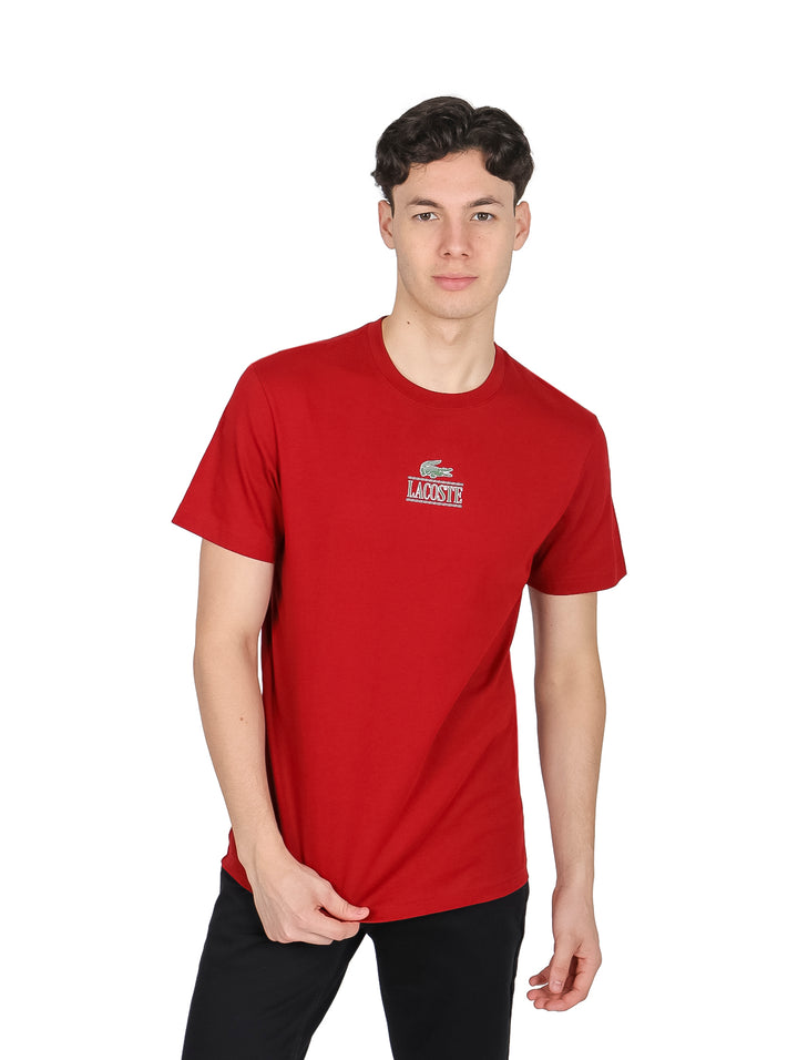 Hombre vistiendo una camiseta roja de manga corta y cuello redondo de la marca Lacoste.