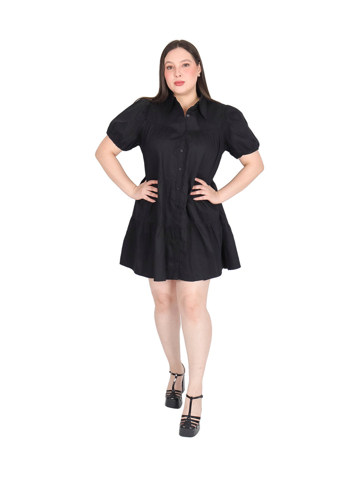 Mujer vistiendo un vestido camisero corto de color negro con botones frontales y mangas cortas.