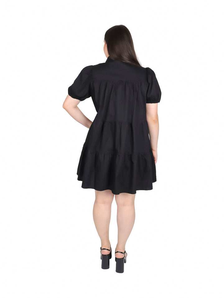 Mujer vistiendo un vestido camisero corto de color negro con botones frontales y mangas cortas.