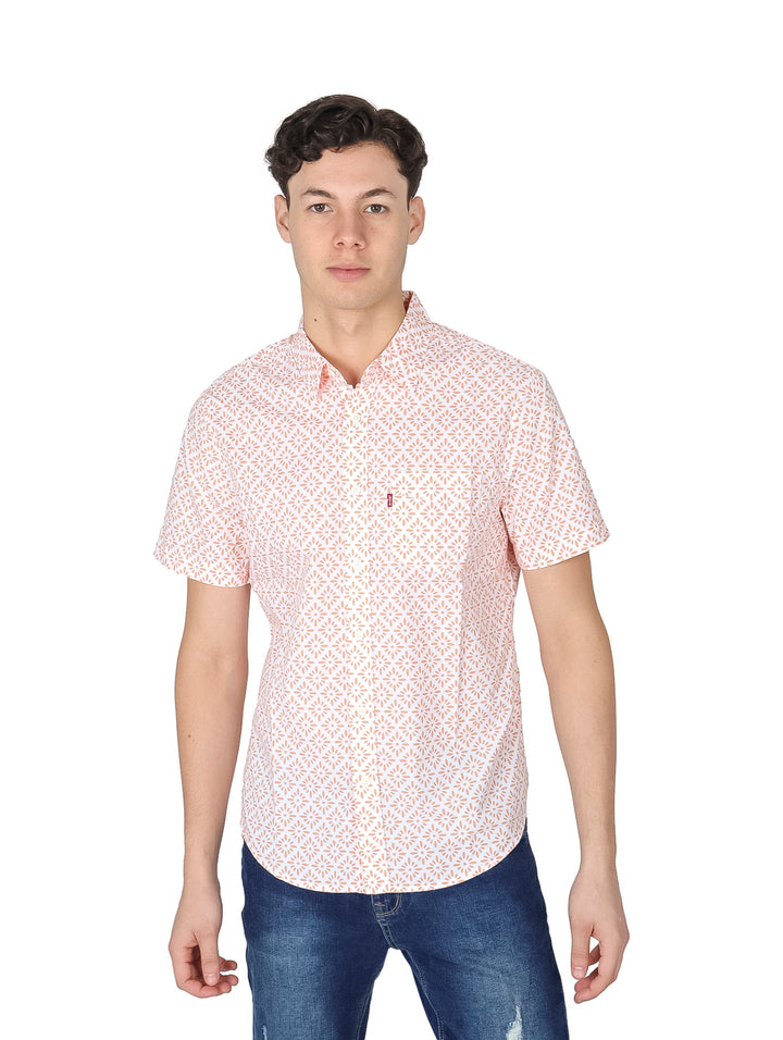 Hombre vistiendo camisa de manga corta blanca con estampado pequeño en color durazno y pantalones vaqueros azules.