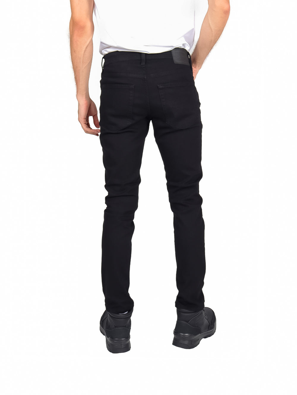 Hombre vistiendo pantalones ajustados de color negro y botas negras sobre fondo blanco.