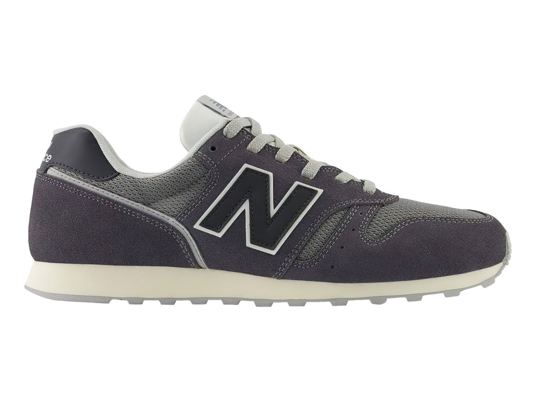 Tenis New Balance color gris oscuro con detalles en malla y suela blanca.