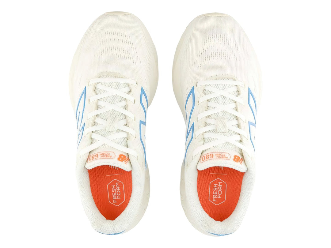 Tenis New Balance 680 color blanco con detalles en azul y suela roja.