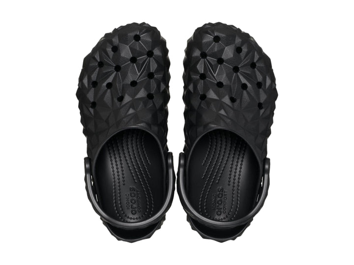 Zueco Crocs negro con relieve geométrico facetado y correa trasera ajustable.