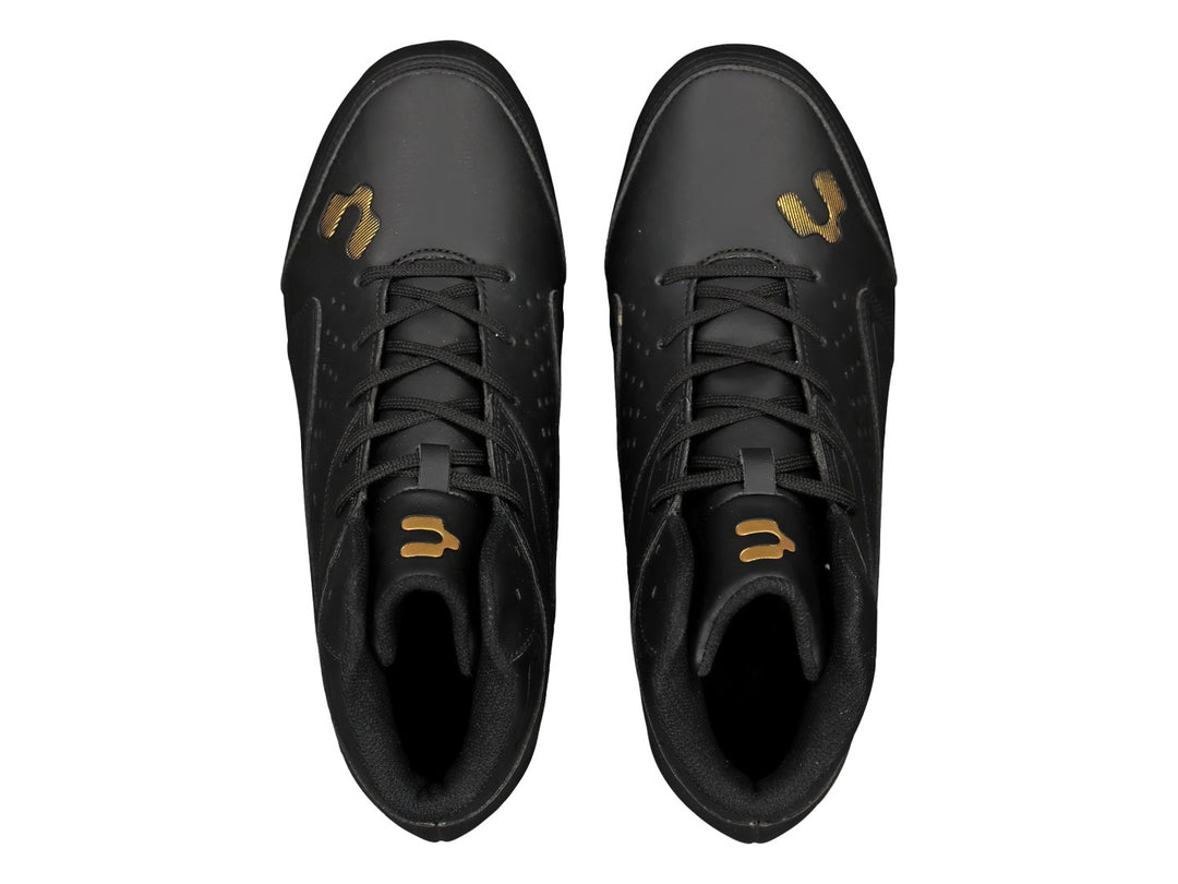Zapato deportivo tipo botín de color negro con suela de tacos dorados.