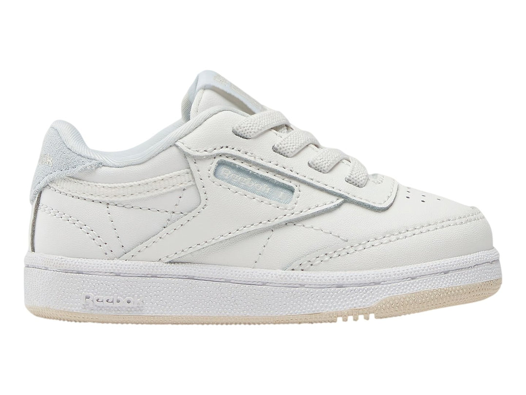 Tenis blancos Reebok Club C para niños con suela color crema y detalles en azul claro.