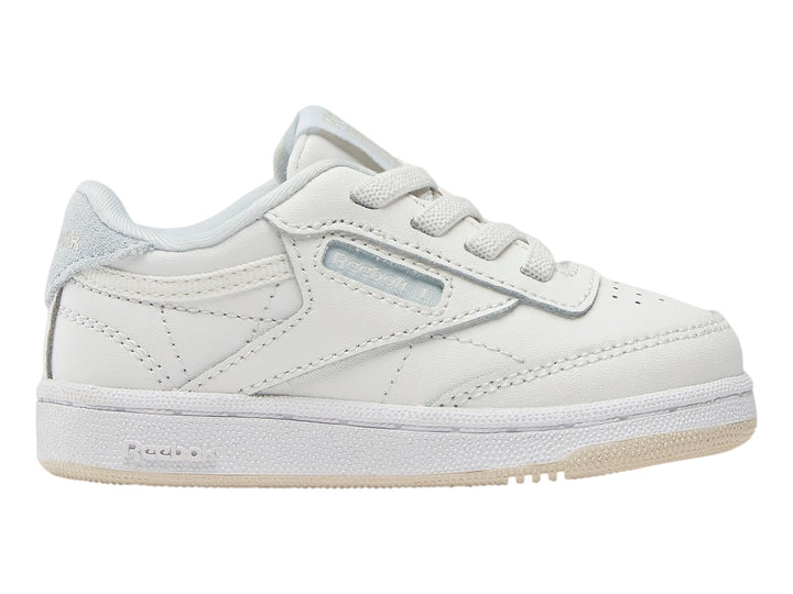 Tenis blancos Reebok Club C para niños con suela color crema y detalles en azul claro.