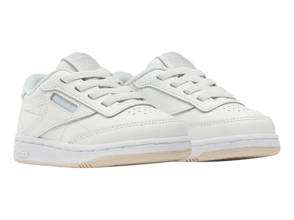 Tenis blancos Reebok Club C para niños con suela color crema y detalles en azul claro.