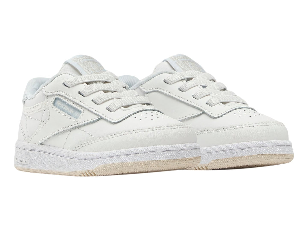 Tenis blancos Reebok Club C para niños con suela color crema y detalles en azul claro.