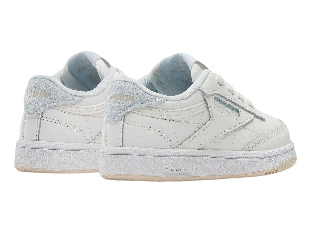 Tenis blancos Reebok Club C para niños con suela color crema y detalles en azul claro.