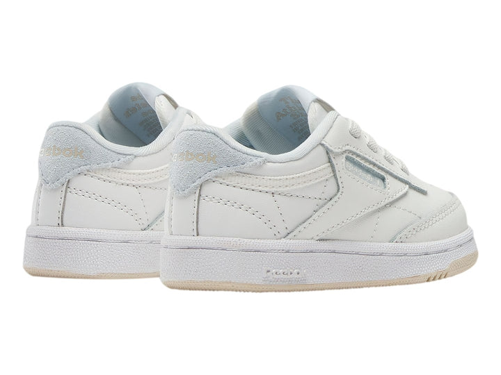 Tenis blancos Reebok Club C para niños con suela color crema y detalles en azul claro.