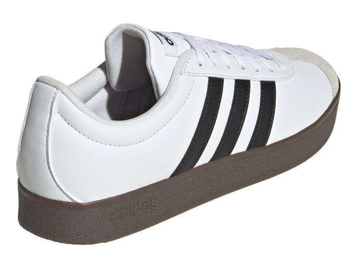 Tenis Adidas blancos con tres rayas negras, punta gris y suela marrón.