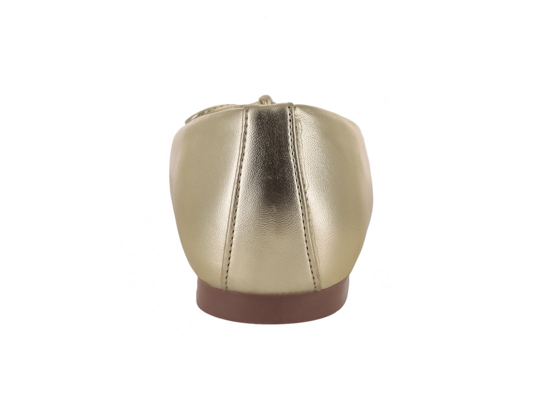 Zapato plano tipo baleta en color oro metálico con detalle de moño decorativo en la parte frontal.