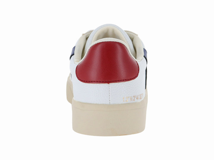 Tenis blancos con franja azul lateral, detalle rojo en el talón y suela beige.
