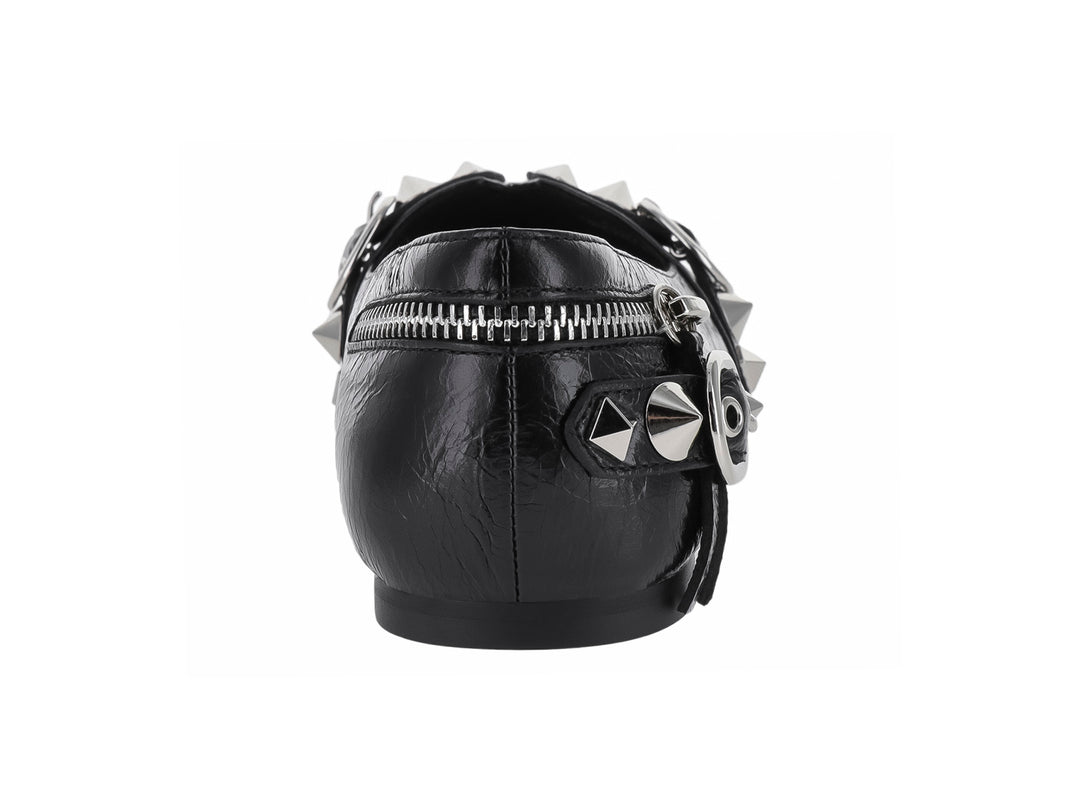 Zapato plano negro de punta afilada con detalles decorativos de cierres, anillos y tachuelas plateadas.