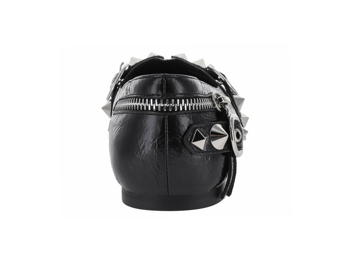 Zapato plano negro de punta afilada con detalles decorativos de cierres, anillos y tachuelas plateadas.