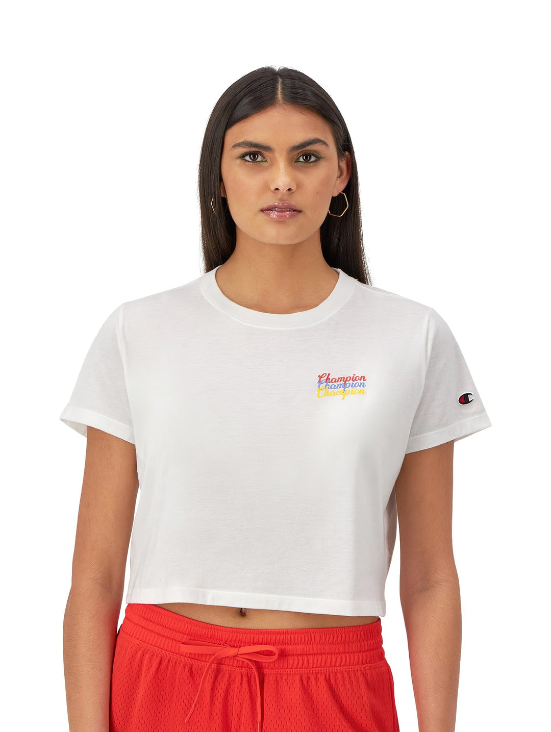 Mujer vistiendo una camiseta blanca corta de marca Champion con logotipo colorido en el pecho.