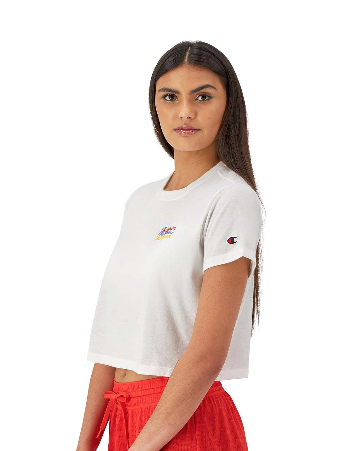 Mujer vistiendo una camiseta blanca corta de marca Champion con logotipo colorido en el pecho.