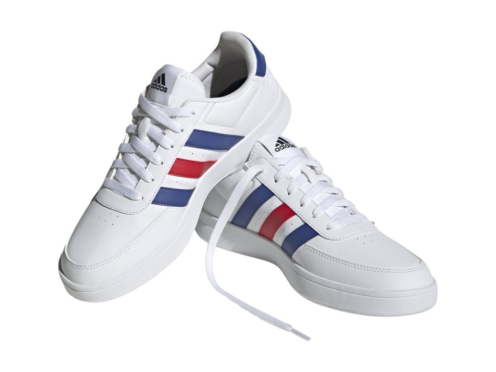 Tenis Adidas blancos con tres franjas laterales en azul y rojo y suela blanca.