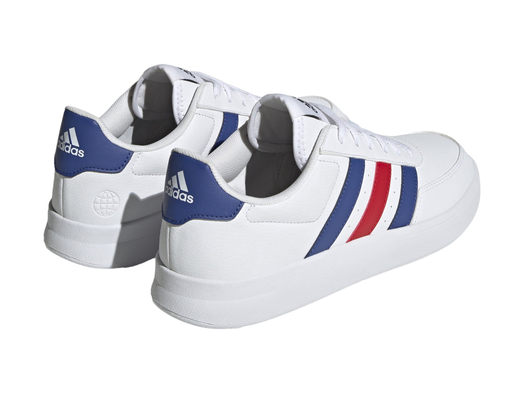 Tenis Adidas blancos con tres franjas laterales en azul y rojo y suela blanca.