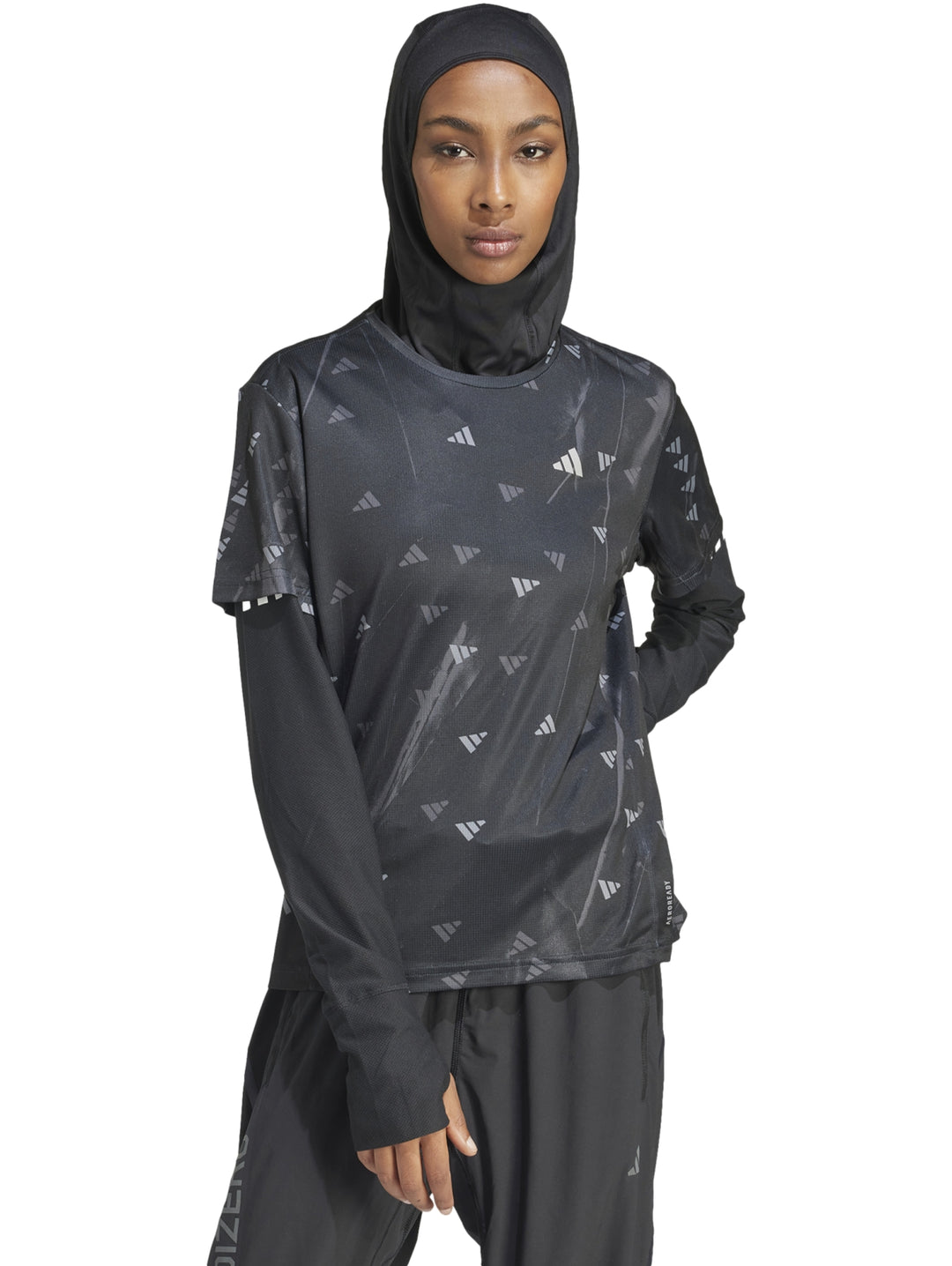 Mujer vistiendo camiseta deportiva Adidas negra de manga larga con estampado sutil y hiyab negro.