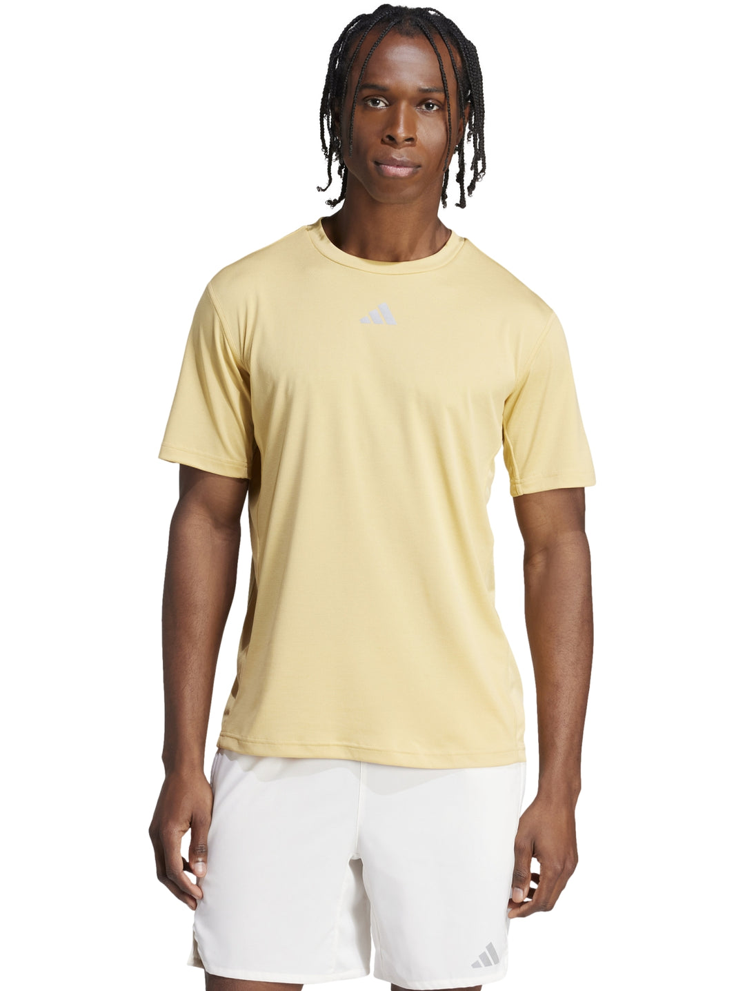 Hombre vistiendo una camiseta deportiva Adidas de color beige claro y shorts blancos.