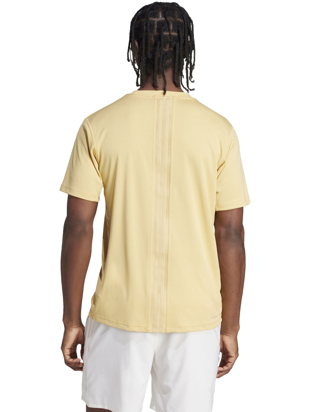 Hombre vistiendo una camiseta deportiva Adidas de color beige claro y shorts blancos.