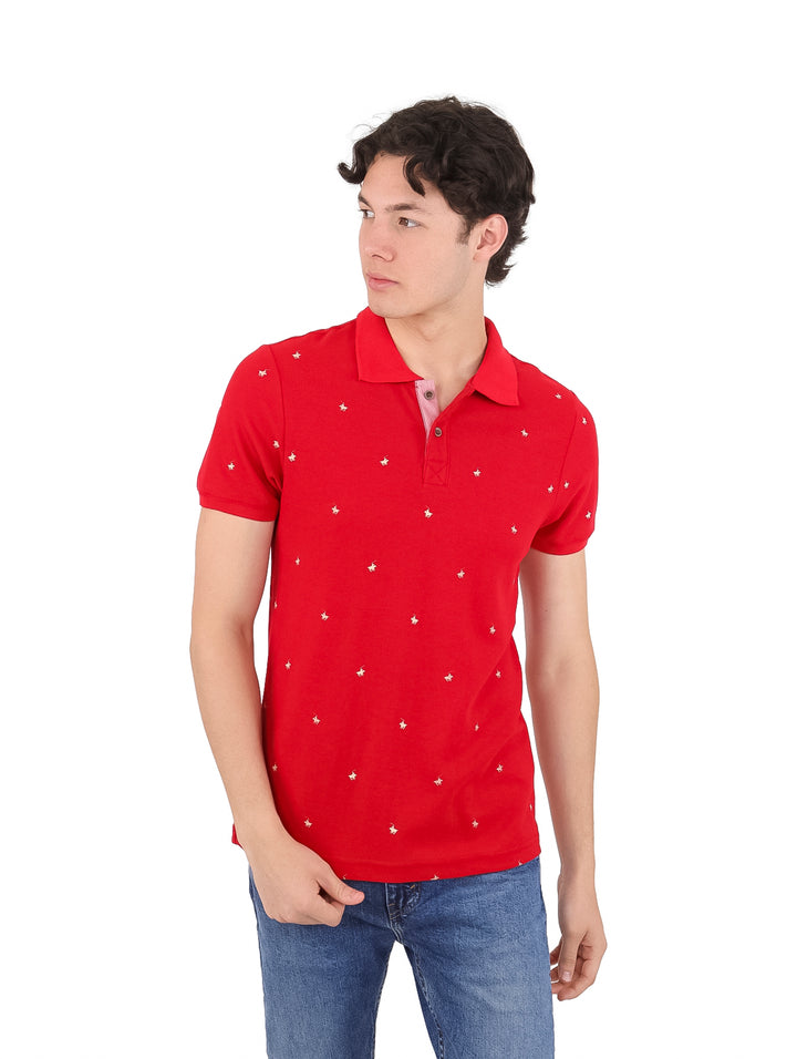 Hombre vistiendo playera polo color rojo con pequeños detalles blancos y pantalones de mezclilla azules.
