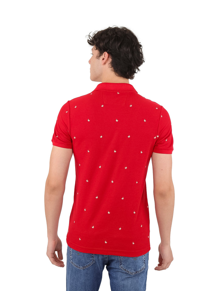 Hombre vistiendo playera polo color rojo con pequeños detalles blancos y pantalones de mezclilla azules.