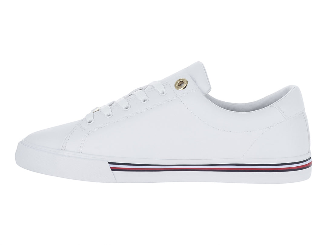 Tenis blancos Tommy Hilfiger estilo court con franjas azul y roja en la suela y logotipo dorado.