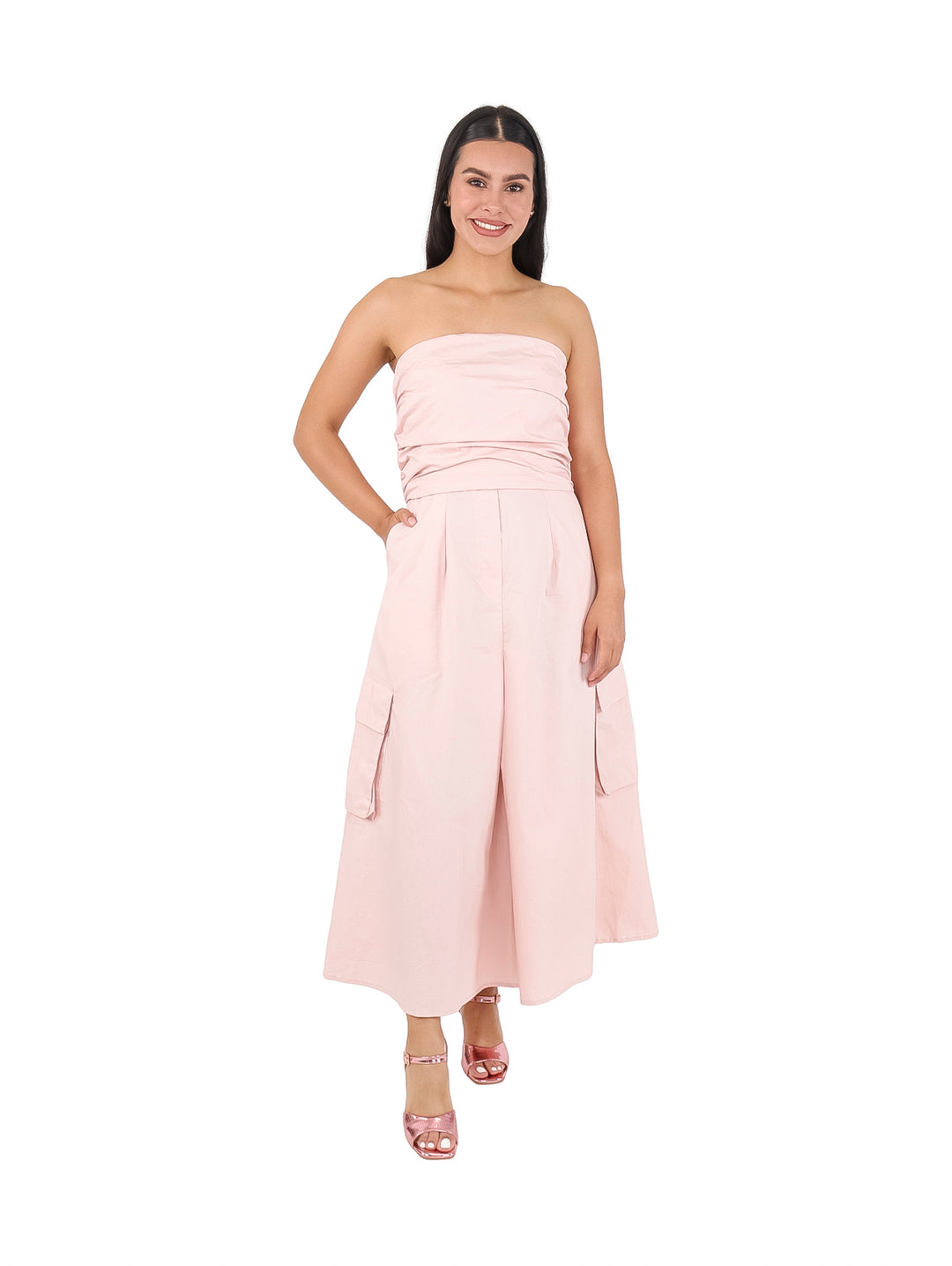 Mujer vistiendo un vestido strapless color rosa claro de largo midi con bolsillos laterales.
