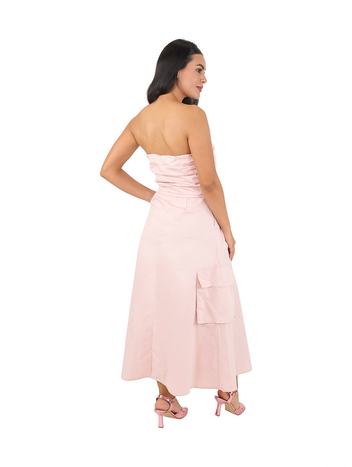 Mujer vistiendo un vestido strapless color rosa claro de largo midi con bolsillos laterales.