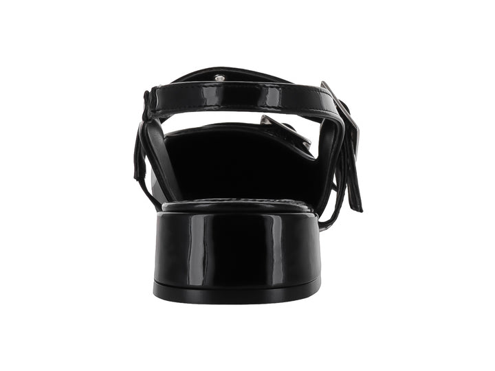 Zapato negro de charol con punta fina, tacón bajo y dos hebillas plateadas.