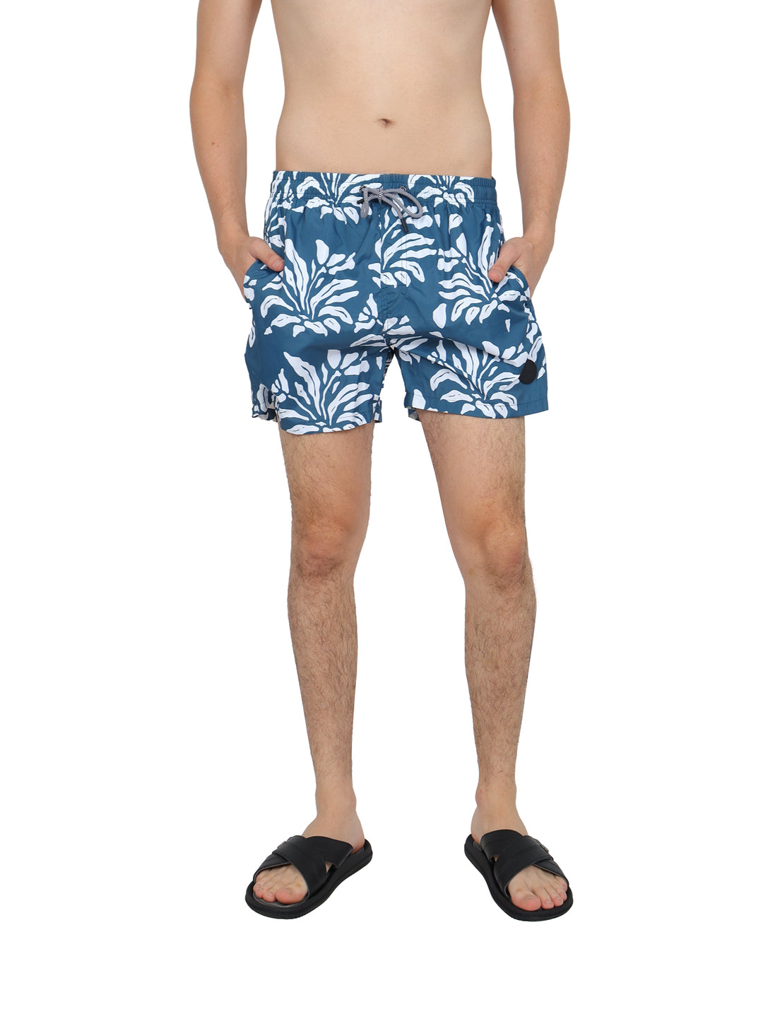 Hombre usando bermudas azules con estampado floral blanco y sandalias negras.