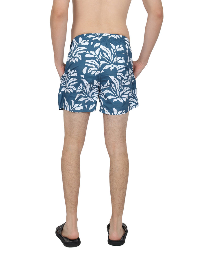 Hombre usando bermudas azules con estampado floral blanco y sandalias negras.