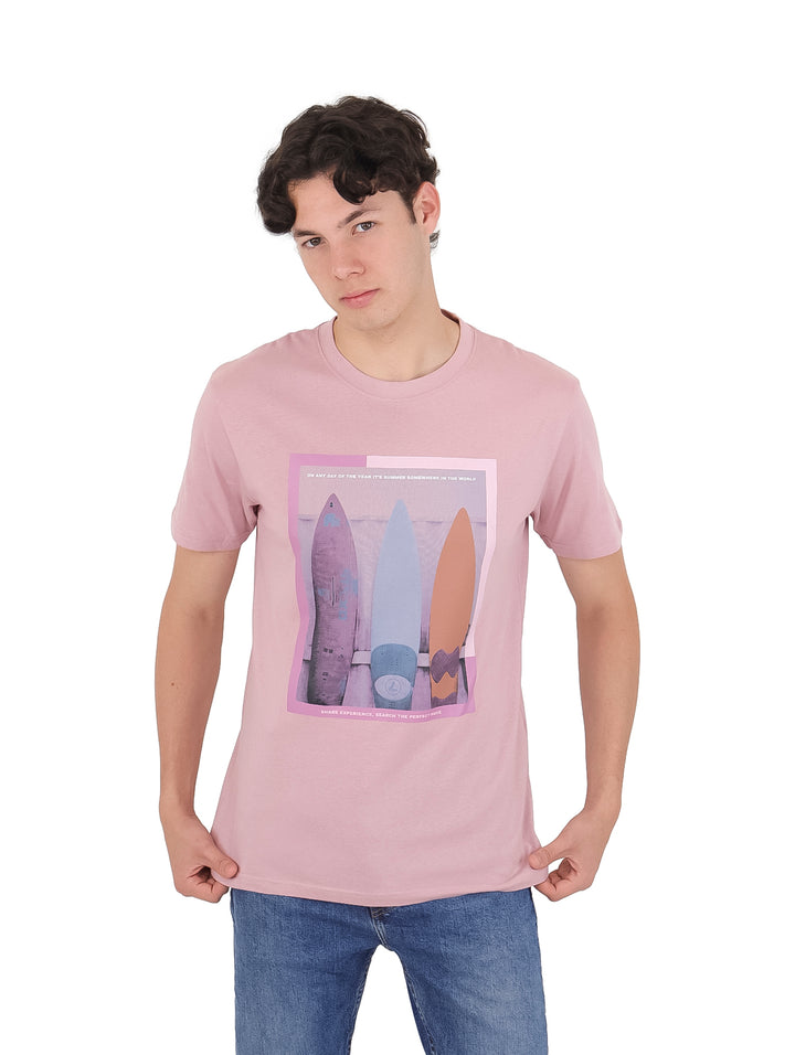 Hombre vistiendo playera rosa claro de manga corta con estampado de tablas de surf en el pecho.
