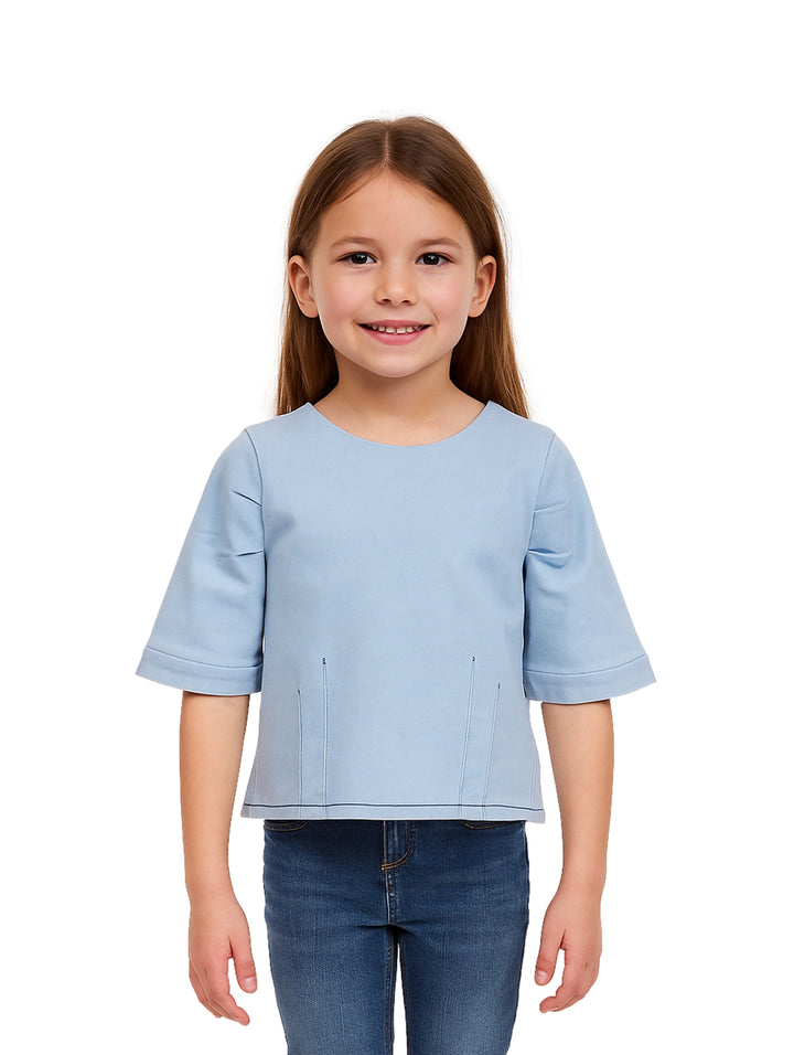Niña vistiendo una blusa de manga corta color azul claro light denim y pantalones de mezclilla.