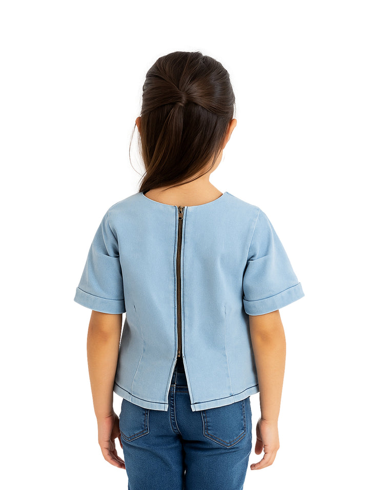 Niña vistiendo una blusa de manga corta color azul claro light denim y pantalones de mezclilla.