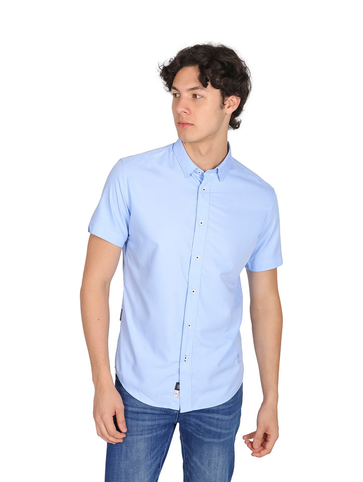 Hombre vistiendo una camisa de manga corta color azul claro y pantalones de mezclilla.